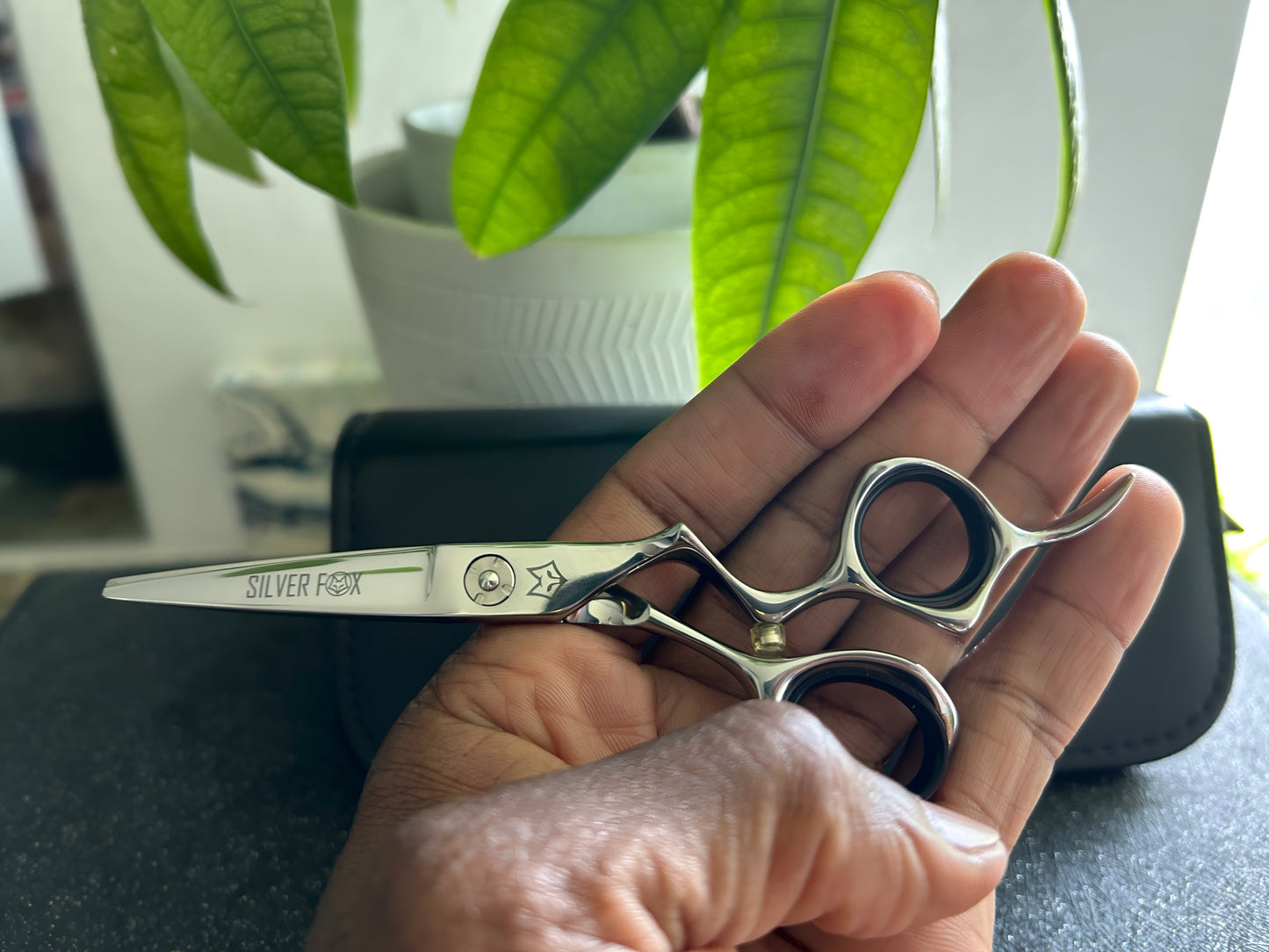 Frontal view of Silver Fox Scissors Model SF28 being held sideways in the left hand, above a display case.