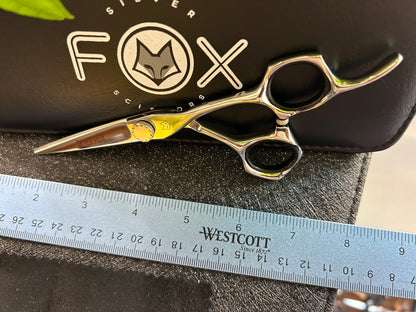 Scissors resting against black case with ruler for scale.