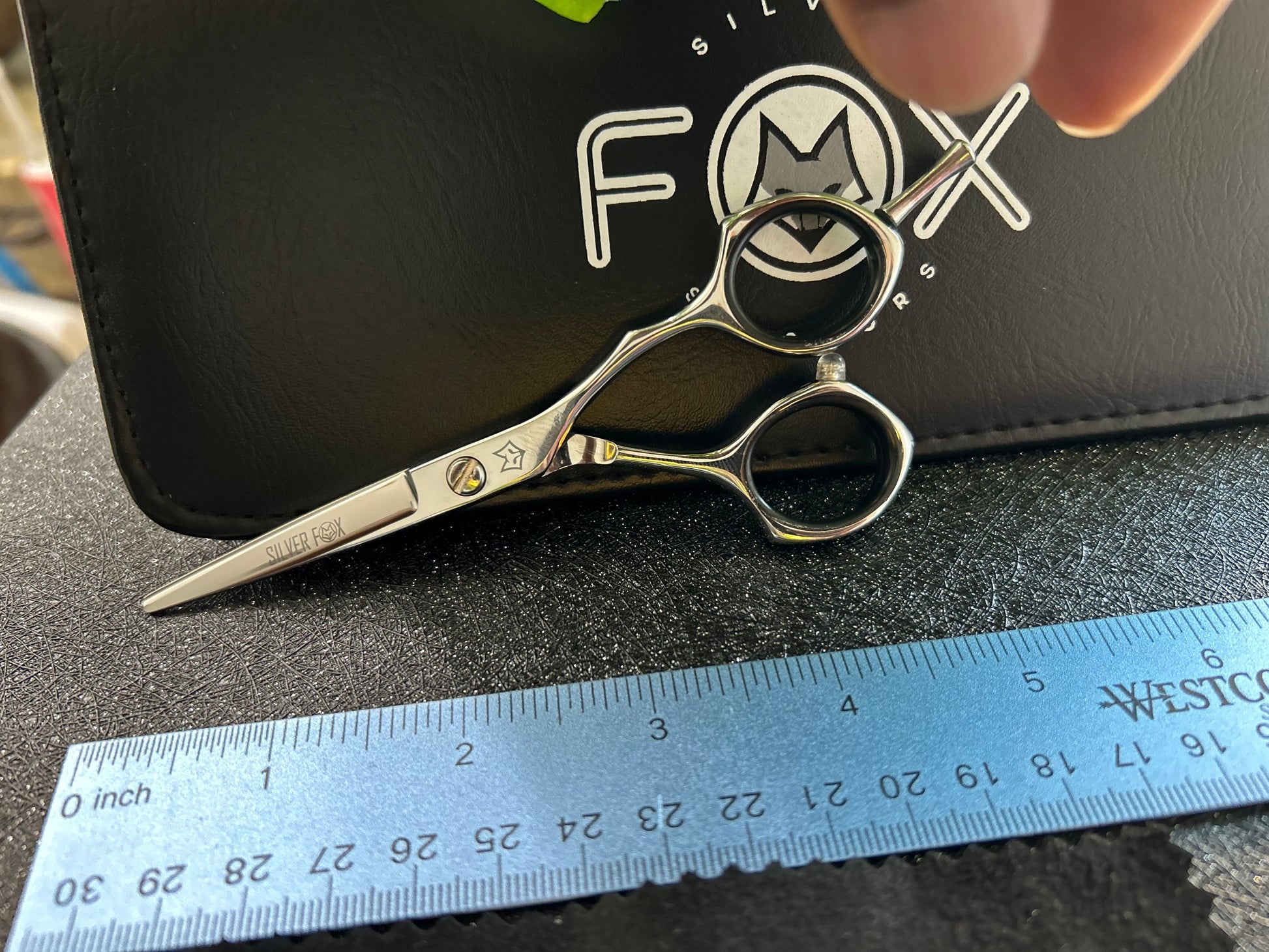 Scissors resting against black case with ruler for scale