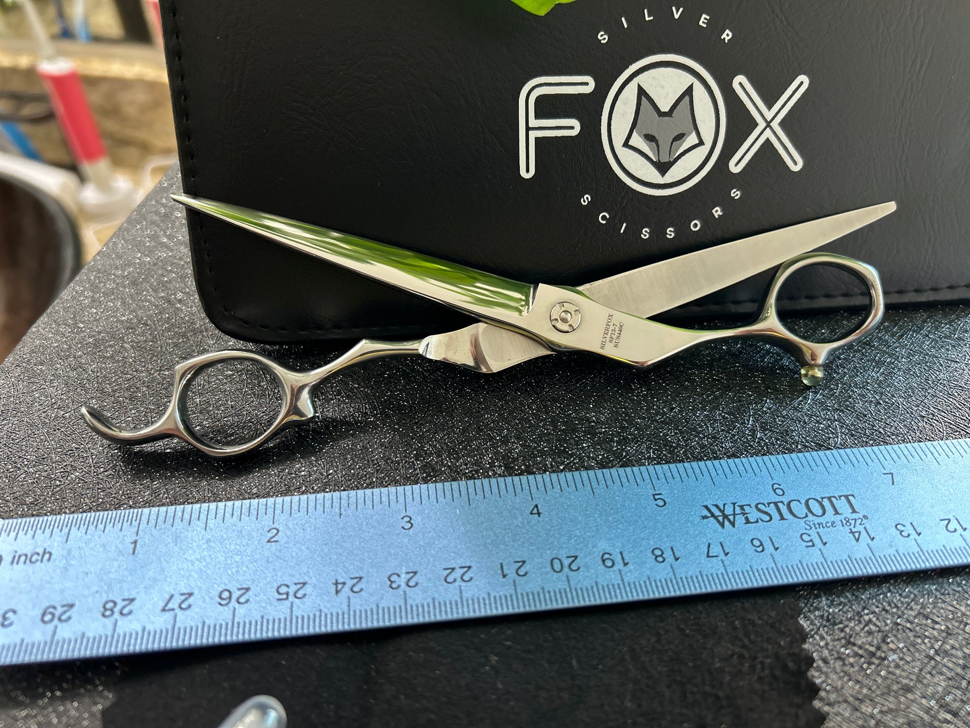 Scissors fully extended resting against black case with ruler for scale.