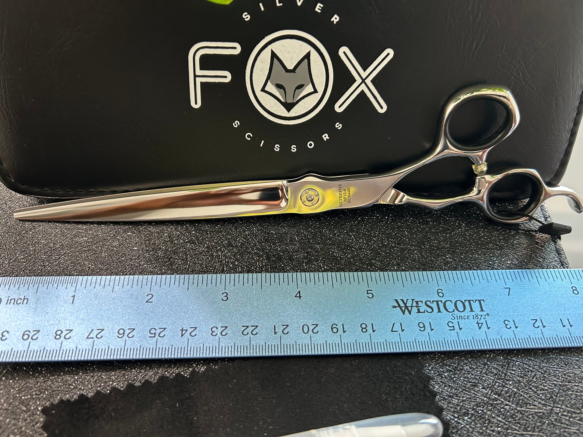 Scissors resting against black case with ruler for scale.