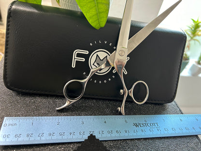 Scissors standing upright against black case with object in front for scale.