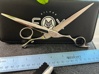 Scissors standing upright, fully extended against black case with ruler in front for scale.