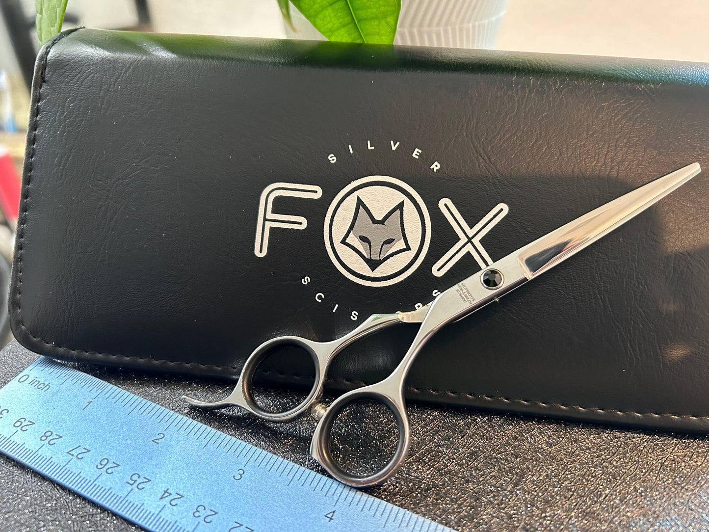 Scissors standing upright against black case with object in front for scale.