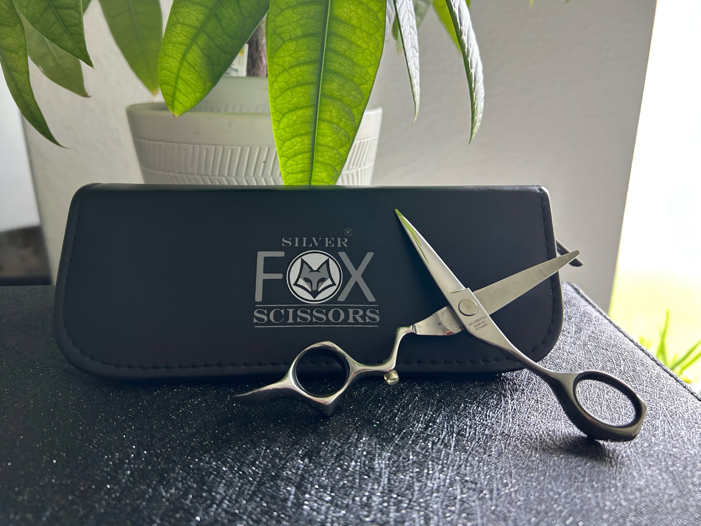 Frontal view of Silver Fox Scissors Model SF28 resting upright against the carrying case, on top of a display case.