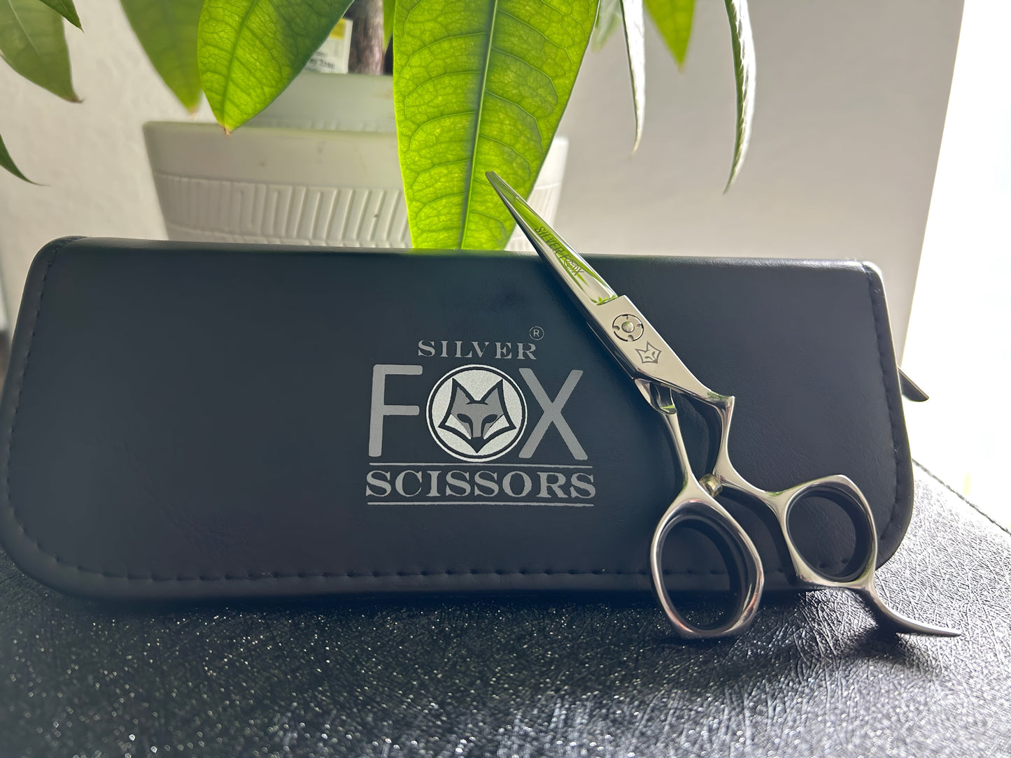 Frontal view of Silver Fox Scissors Model SF28 resting upright against the carrying case, on top of a display case.