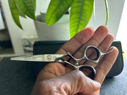 Frontal view of Silver Fox Scissors Model SF28 being held sideways in the left hand, above a display case. 