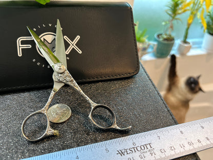 Scissors standing upright against black case with object in front for scale.